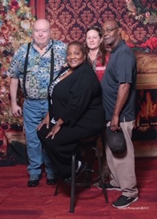 4 people posing in front of holiday backdrop with fireplace and Christmas tree